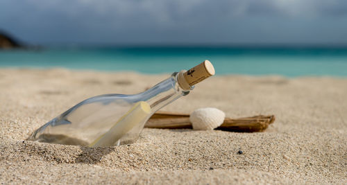 Close-up of message in a bottle on beach against sky