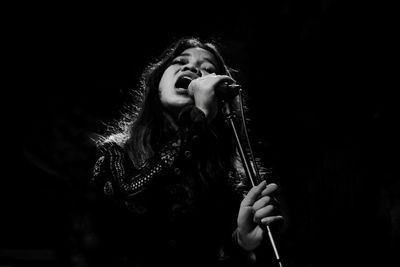 Young woman singing while holding microphone in darkroom