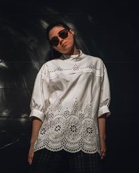 Young woman wearing sunglasses standing against wall