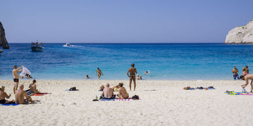 People at beach against clear blue sky