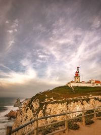 Lighthouse by mountain against sky