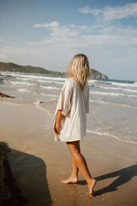 Rear view of woman standing at beach against sky