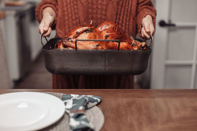 Midsection of person preparing food on table at home. roasted turkey on metal tray