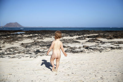 Rear view of naked baby girl boy walking at beach