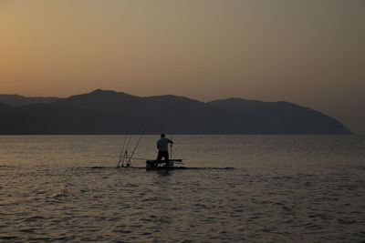 Silhouette man on boat in sea against sky during sunset