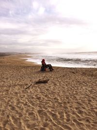 Boy sitting on sand at beach against sky