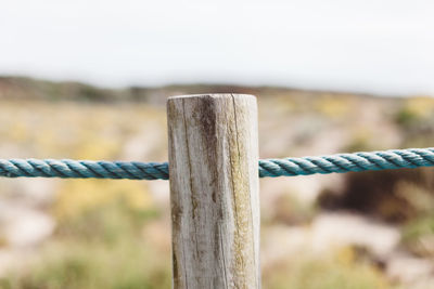 Close-up of wooden post by rope against sky
