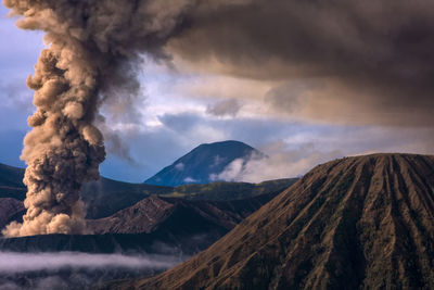 Smoke emitting from volcano against cloudy sky