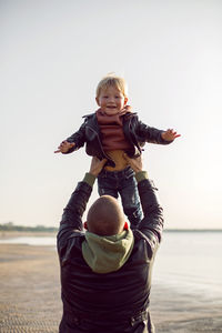 Father and son in leather jackets in autumn walking in nature near the bay on the beach with sand