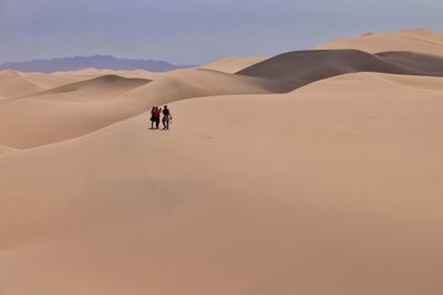 People walking on desert against clear sky