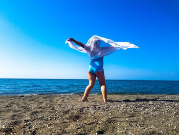 Full length of girl standing at beach against blue sky