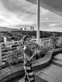 Young woman standing by buildings against sky in city