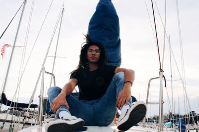 Portrait of beautiful young woman sitting on boat sailing in sea against sky