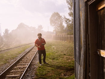 Portrait of man holding camera standing by railroad track