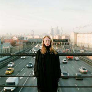 Portrait of young woman standing on bridge in city against sky