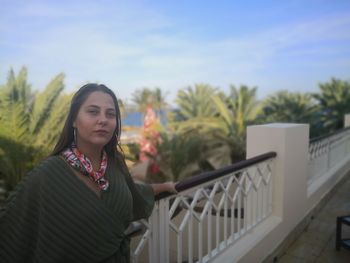 Portrait of woman standing by railing against sky