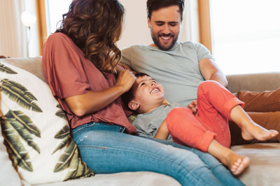 Cheerful parents playing with son on sofa at home