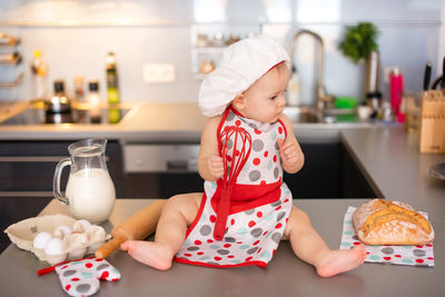 Full length of cute girl holding wire whisk sitting on table at kitchen