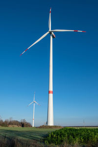 Low angle view of wind turbines on field against clear blue sky
