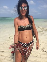 Portrait of smiling woman holding starfish while standing on sand at beach