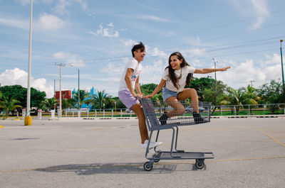 Full length of happy friends with shopping cart on parking lot