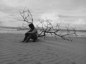 Lonely man sitting on driftwood at sandy beach