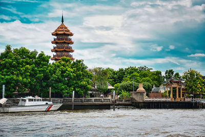 Built structure by river against buildings and trees against sky