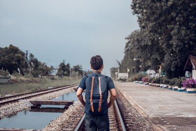 Rear view of man on railroad tracks against sky
