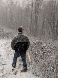 Rear view of man standing in forest during snowfall