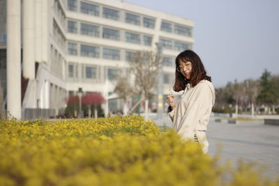 Portrait of smiling young woman standing by plants against building