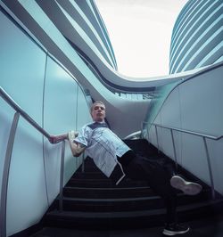 Man on steps leaning by railing against clear sky