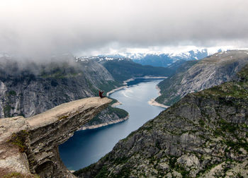 Mid distance of person sitting on cliff against rivercliffdanger