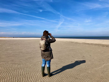Woman looking over the sea with binoculars on a clear day from a beach with ribbed sand