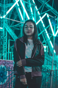 Portrait of young woman standing against illuminated ride at night