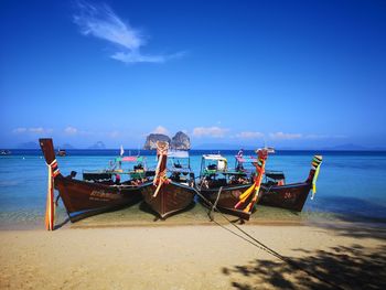 Boats moored on beach against blue sky