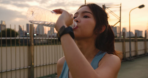 Close-up of young woman drinking water against sky