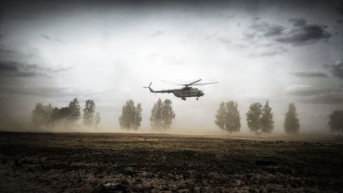 Helicopter flying over field against sky