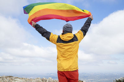 Hiker waving a rainbow lgbt pride flag in high mountains. inclusive sport. mountain activities