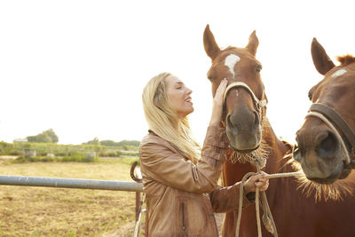 Farmer stroking horse in farm against clear sky