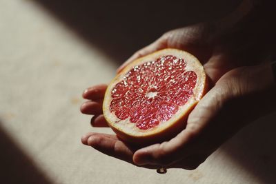 Cropped image of person holding halved grapefruit in sunlight
