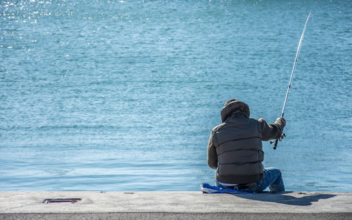 Rear view of man sitting by sea