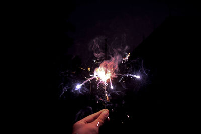 Cropped hand of person holding illuminated sparkler against clear sky at night