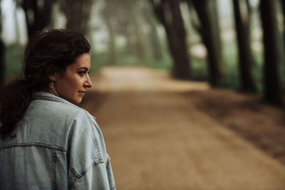 Portrait of a young girl looking aside while standing on forest road