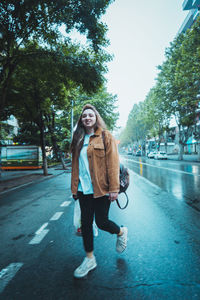 Full length of smiling woman standing on road in city