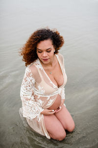 Young pregnant woman kneeling in water at beach