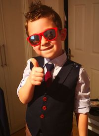Portrait of boy in suit gesturing thumbs up while standing at home