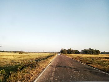 Road amidst field against clear sky