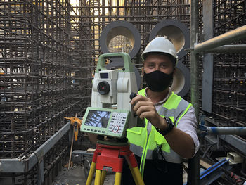 Land surveyor dressed in hardhat, mask and protective vest works on total station. geodetic engineer 