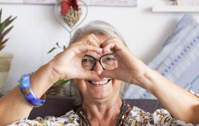 Portrait of smiling woman making heart shape sitting at home