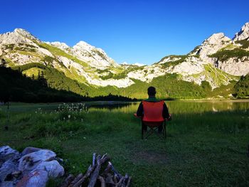 Rear view of man sitting on chair by lake against sky